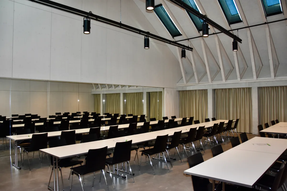 Im Kurssaal stehen die Tische und Stühle ebenfalls für Veranstaltungen bereit. Tische und Stühle stehen aufgereiht in einem Raum.